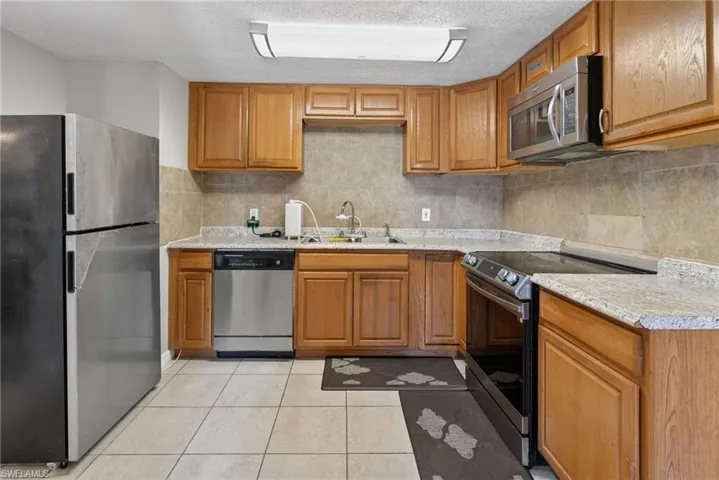 Kitchen featuring stainless steel appliances, light countertops, wood finish cabinetry, and a textured ceiling