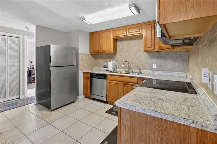 Kitchen with stainless steel appliances, light countertops, wood finish cabinetry, light tile patterned flooring, and a textured ceiling