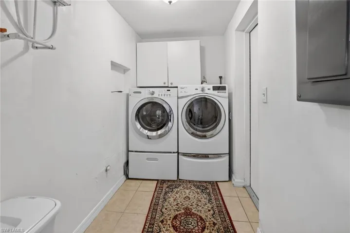 Laundry area with cabinet space, electric panel, light tile patterned floors, and washer and dryer