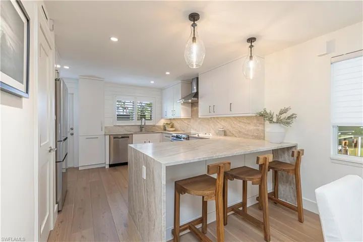 Kitchen featuring stainless steel appliances, a peninsula, white cabinets, wall chimney range hood, and pendant lighting