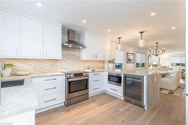 Kitchen with beverage cooler, wall chimney exhaust hood, appliances with stainless steel finishes, open floor plan, and a peninsula