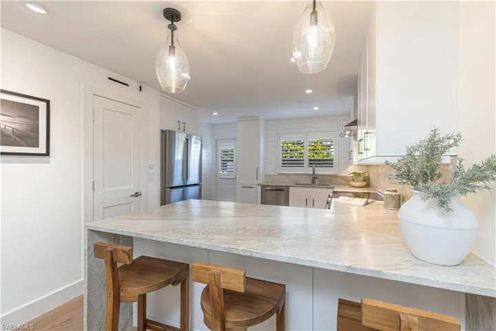 Kitchen featuring decorative light fixtures, a breakfast bar area, appliances with stainless steel finishes, white cabinets, and a peninsula
