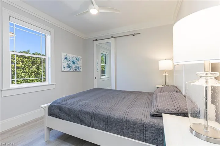 Bedroom featuring hardwood / wood-style flooring, ceiling fan, a barn door, and crown molding