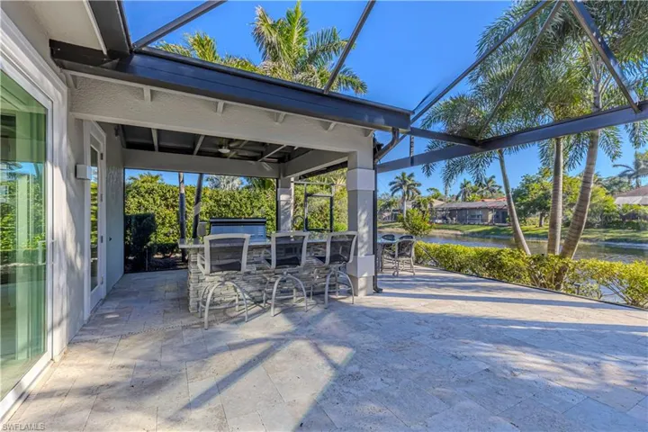 View of patio / terrace with glass enclosure, a water view, exterior bar, ceiling fan, and exterior kitchen