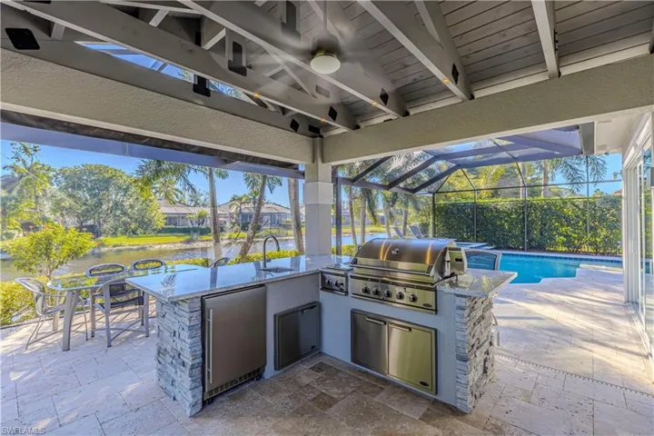 View of patio with area for grilling, a lanai, a wet bar, a water view, and a grill