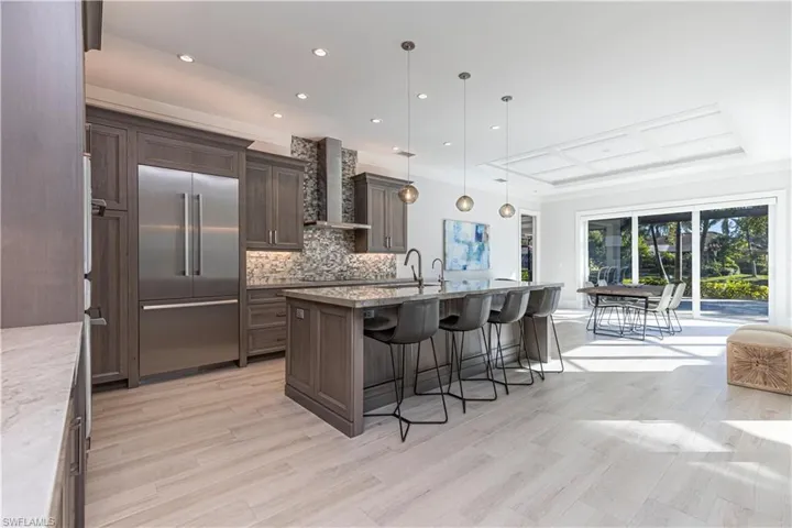 Kitchen with decorative backsplash, wall chimney range hood, stainless steel built in fridge, hanging light fixtures, and a breakfast bar area