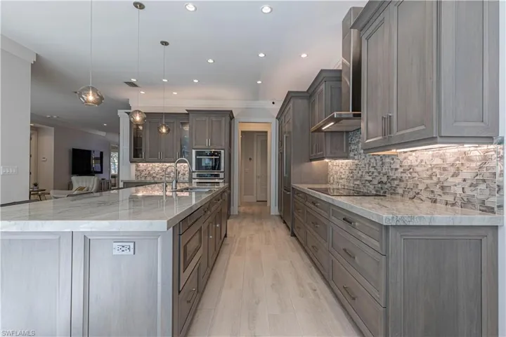 Kitchen featuring pendant lighting, wall chimney range hood, tasteful backsplash, a large island, and light stone counters