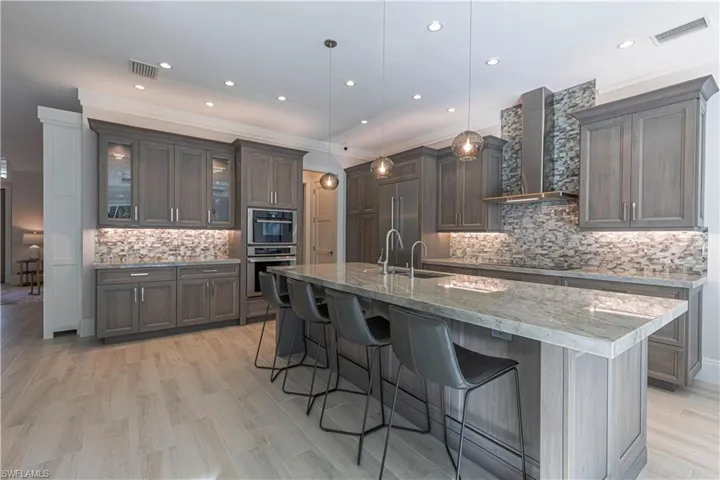 Kitchen with light stone countertops, sink, wall chimney range hood, a large island with sink, and hanging light fixtures