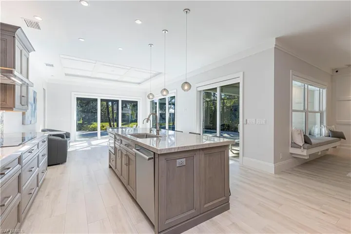 Kitchen featuring pendant lighting, dishwasher, a kitchen island with sink, sink, and light stone countertops