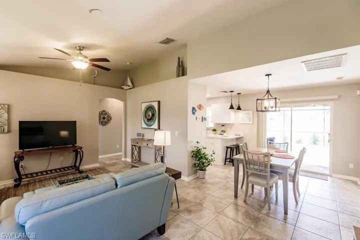 Tiled living room featuring ceiling fan with notable chandelier and vaulted ceiling