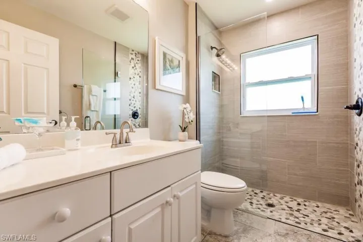 Bathroom featuring a tile shower, vanity, and toilet
