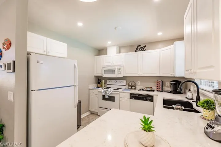 Kitchen with light stone countertops, white cabinets, white appliances, and sink
