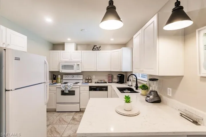 Kitchen featuring white cabinets, decorative light fixtures, sink, and white appliances
