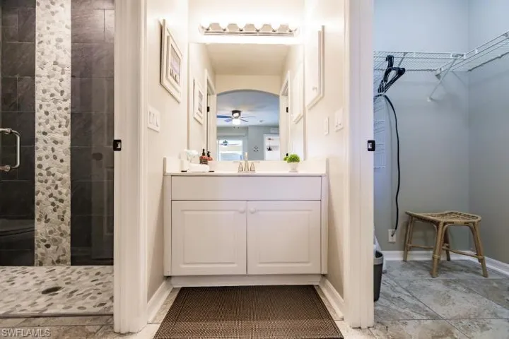 Bathroom with a tile shower, ceiling fan, and vanity