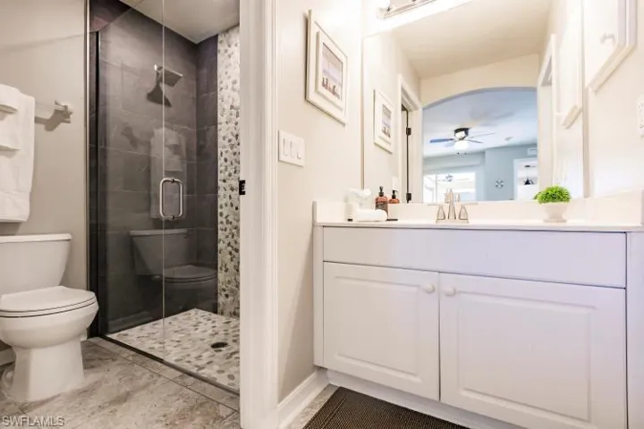 Bathroom with ceiling fan, vanity, an enclosed shower, tile patterned floors, and toilet