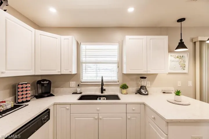 Kitchen featuring sink, white cabinets, hanging light fixtures, light stone countertops, and stainless steel dishwasher