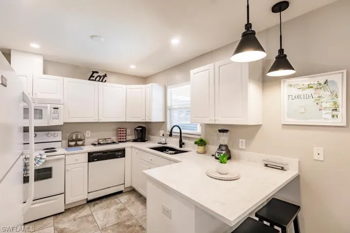 Kitchen with sink, white cabinets, kitchen peninsula, white appliances, and decorative light fixtures