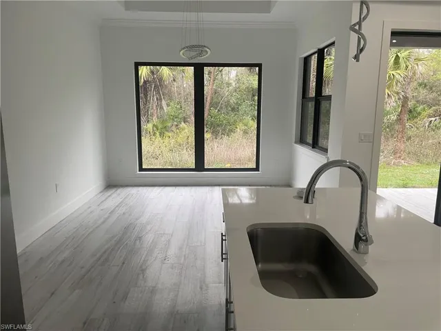 Kitchen with light wood-type flooring, a tray ceiling, light stone counters, white cabinets, and hanging light fixtures