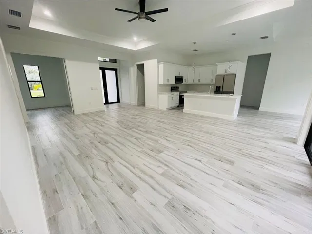 Unfurnished living room with ceiling fan, a tray ceiling, light wood-type flooring, recessed lighting, and crown molding