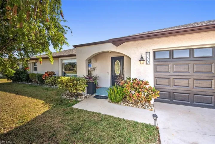 Doorway to property featuring a garage, stucco siding, a lawn, and driveway