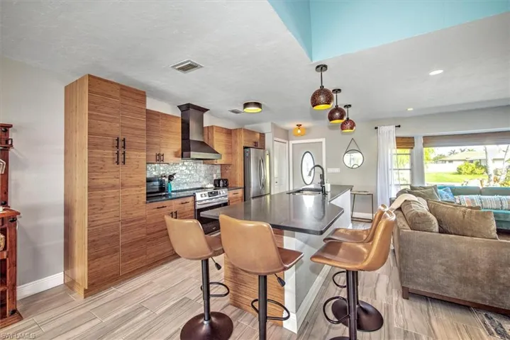 Kitchen featuring open floor plan, wood finish cabinetry, a breakfast bar, stainless steel appliances, and a kitchen island with sink