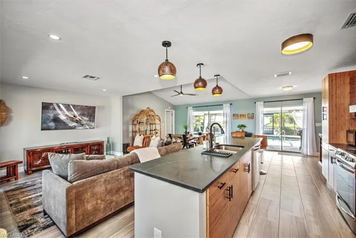 Kitchen with open floor plan, stainless steel appliances, pendant lighting, an island with sink, and vaulted ceiling