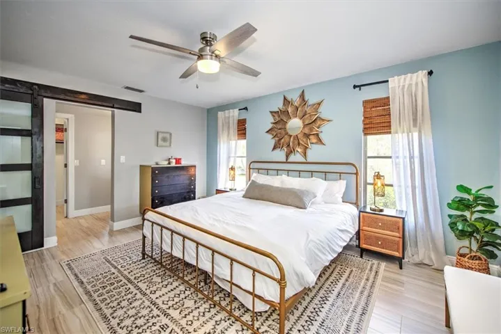 Bedroom featuring a barn door, ceiling fan, and light wood-style floors
