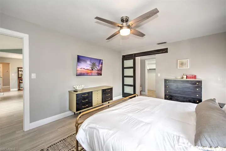 Bedroom with a barn door, light wood-style floors, and a ceiling fan