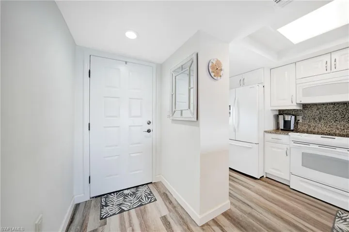 Kitchen featuring light hardwood / wood-style flooring, white appliances, backsplash, and white cabinetry