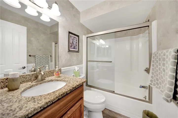 Full bathroom with toilet, hardwood / wood-style flooring, vanity, and bath / shower combo with glass door