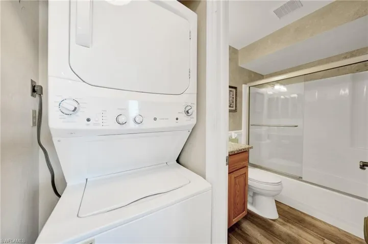 Laundry area with hardwood / wood-style flooring and stacked washing maching and dryer