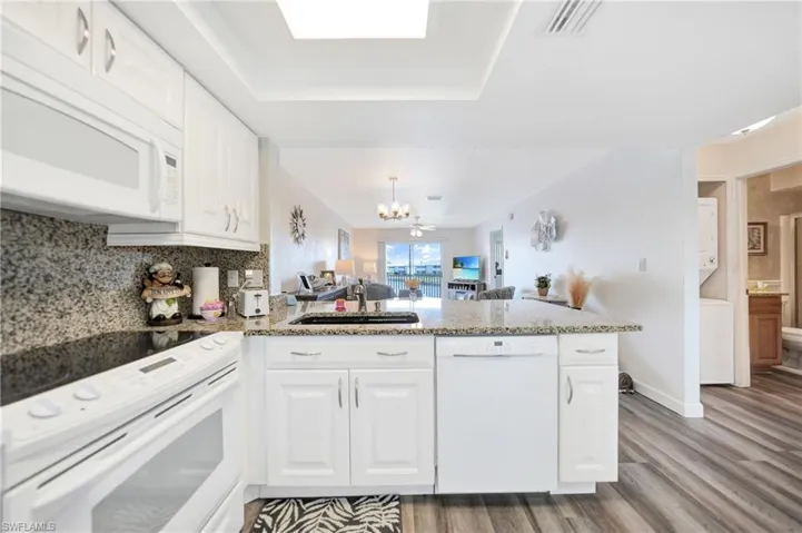 Kitchen with white cabinetry, kitchen peninsula, light wood-type flooring, white appliances, and sink