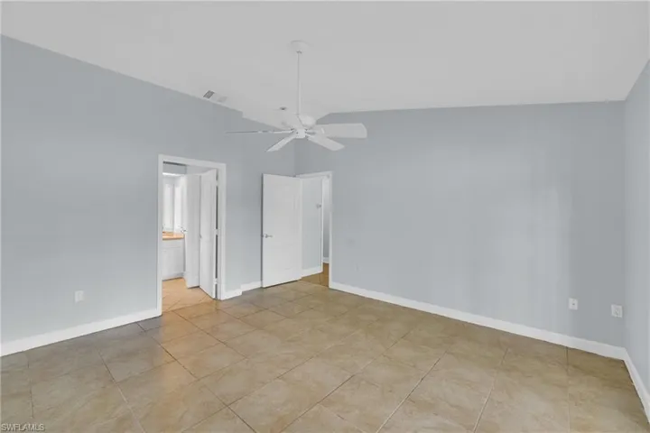 Unfurnished bedroom featuring vaulted ceiling, light tile patterned flooring, ensuite bath, and a ceiling fan