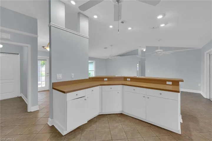 Kitchen with ceiling fan, light tile patterned floors, vaulted ceiling, white cabinets, and a peninsula