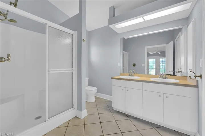 Bathroom with a stall shower, double vanity, tile patterned flooring, and a ceiling fan
