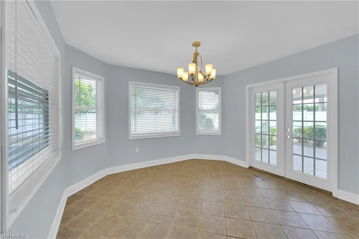 Tiled spare room featuring a chandelier and french doors