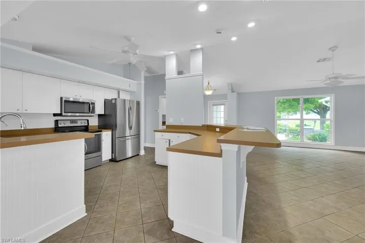 Kitchen featuring ceiling fan, appliances with stainless steel finishes, light tile patterned floors, vaulted ceiling, and a peninsula