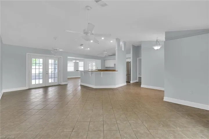 Unfurnished living room with a ceiling fan, vaulted ceiling, light tile patterned floors, and french doors
