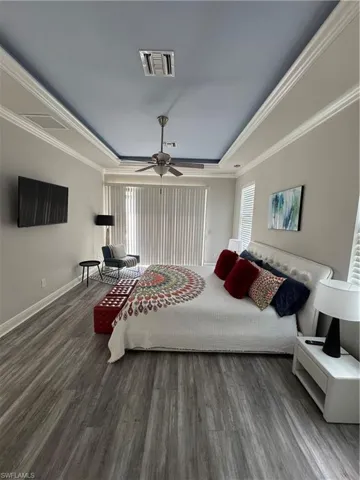 Bedroom with a raised ceiling, wood finished floors, ceiling fan, and crown molding