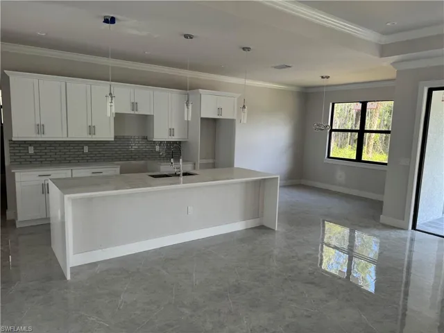 Kitchen with decorative backsplash, white cabinetry, ornamental molding, and a kitchen island