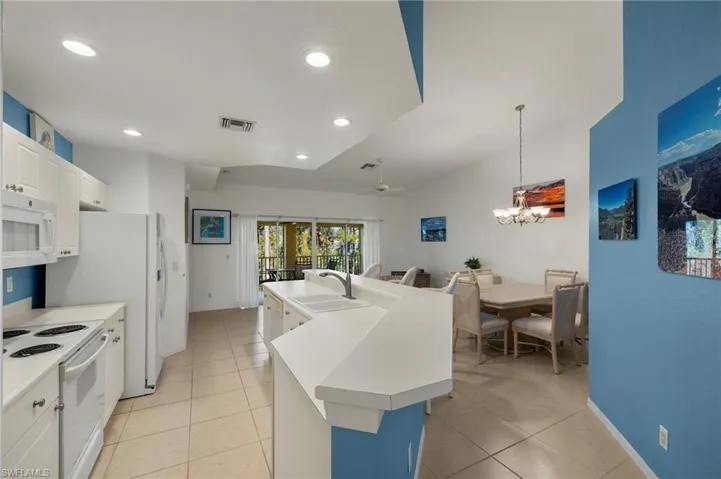 Kitchen featuring sink, lofted ceiling, white appliances, a kitchen island with sink, and white cabinets