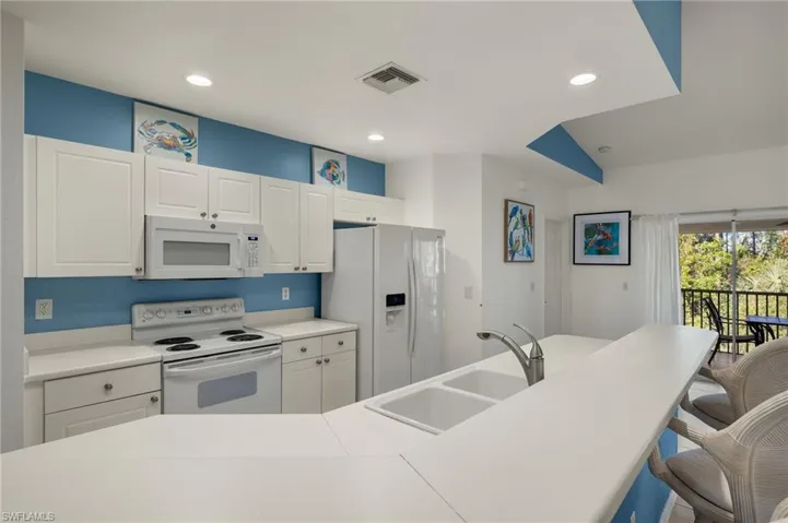 Kitchen with white cabinets, white appliances, a breakfast bar area, and sink