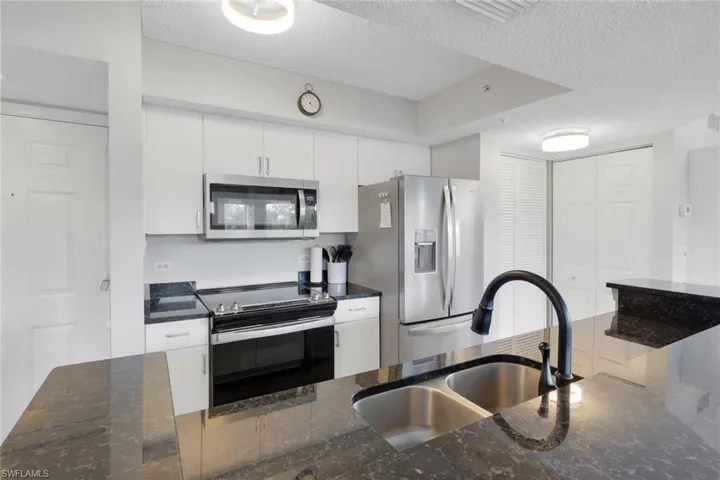 Kitchen with dark stone counters, stainless steel appliances, a textured ceiling, and white cabinetry