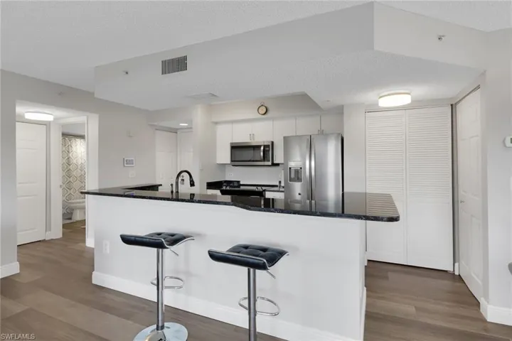 Kitchen with stainless steel appliances, a textured ceiling, dark wood-style floors, a breakfast bar, and white cabinets