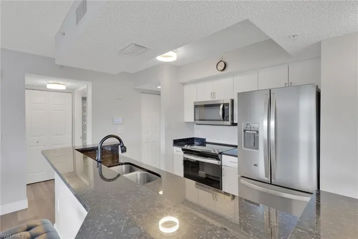 Kitchen with stainless steel appliances, dark stone countertops, white cabinetry, a textured ceiling, and light wood-style flooring