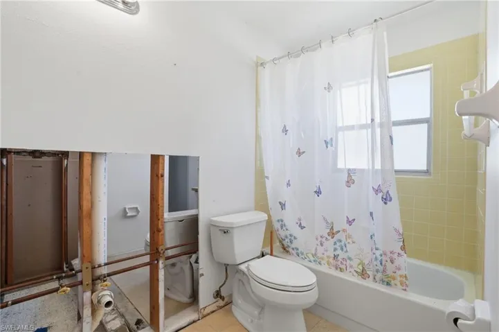 Bathroom with shower / bathtub combination with curtain and toilet