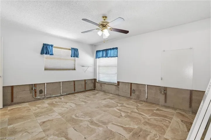 Empty room featuring a textured ceiling, ceiling fan, wainscoting, and tile walls