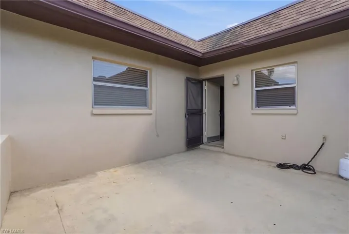 Property entrance featuring stucco siding, a shingled roof, and a patio area
