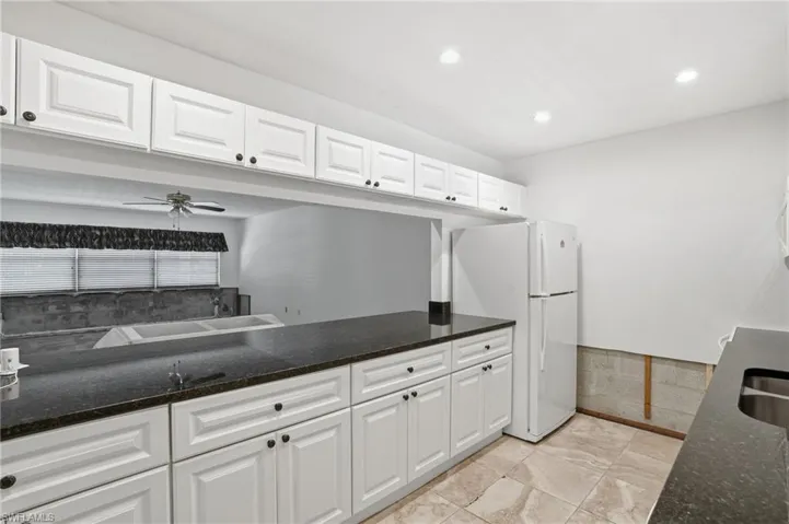 Kitchen featuring white cabinets, dark stone counters, freestanding refrigerator, a ceiling fan, and recessed lighting
