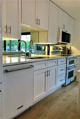 Kitchen with white cabinets, range with two ovens, light countertops, light wood-style floors, and a sink